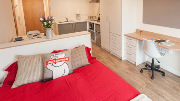 A bedroom with a red bedspread and a white desk with a computer on it.