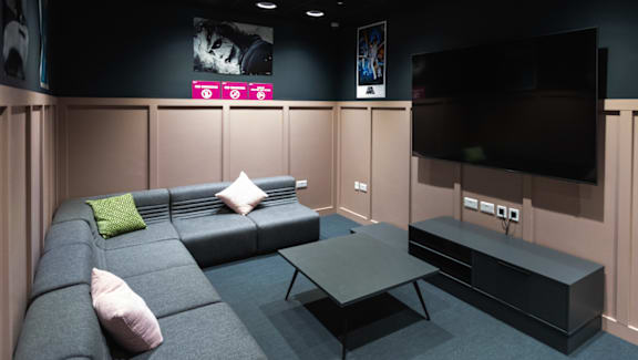 A black TV is mounted on a wall above a grey couch.