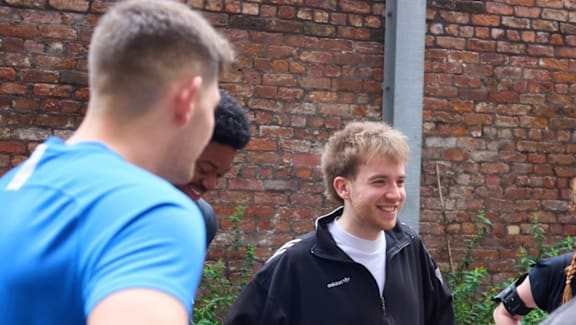 A group of people are standing outside near a brick wall.