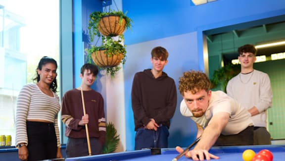A group of people are gathered around a pool table.