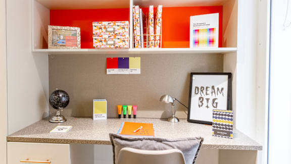 A small desk with a chair and a framed sign that says "Dream Big".
