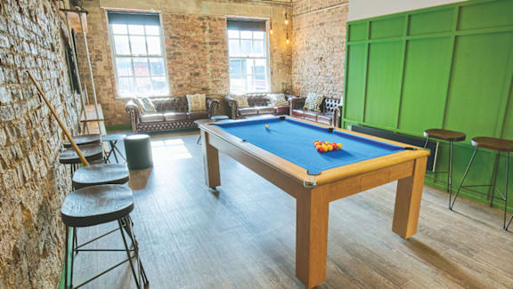 A pool table is in the middle of a room with a brick wall and a green screen.
