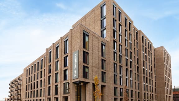 A tall building with a dark brown facade and a green sign on the front.