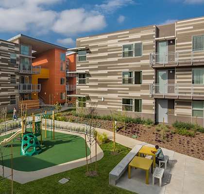 A playground area with a green slide and yellow chairs is in front of a building.