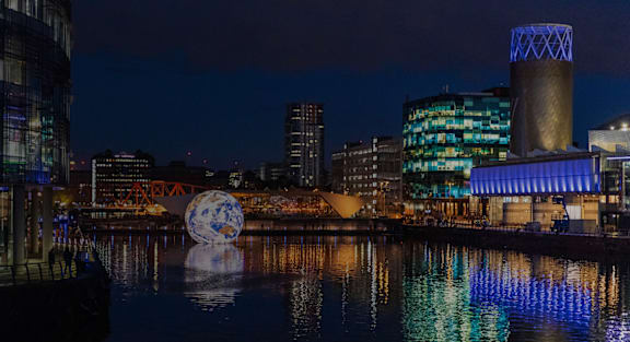 A large globe is reflected in the water in front of a city skyline.