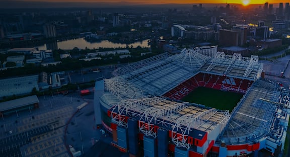 A large stadium with red seats and a roof is shown during sunset.