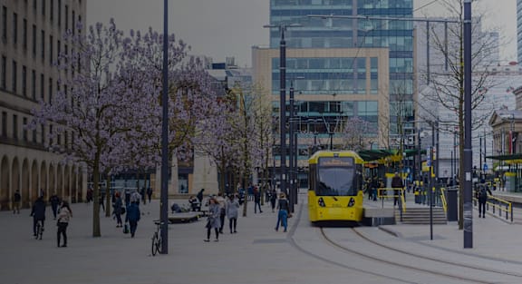 A yellow tram is on a street with people walking on the sidewalk.