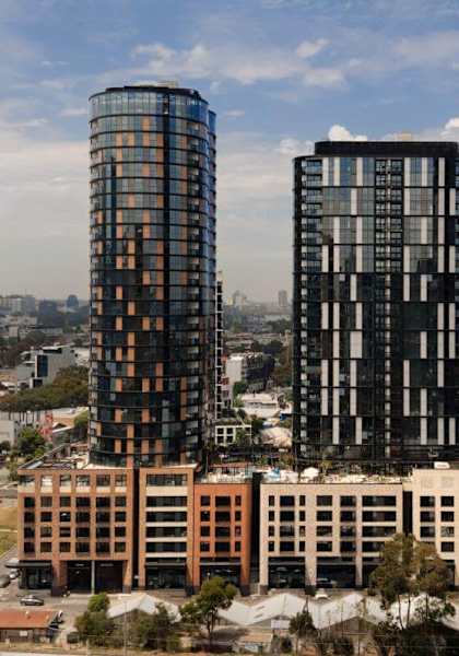 Three tall buildings with glass windows are in the foreground of a cityscape.