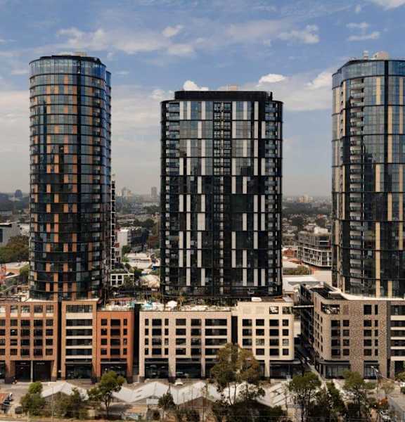 Three tall buildings with glass windows are in the foreground of a cityscape.