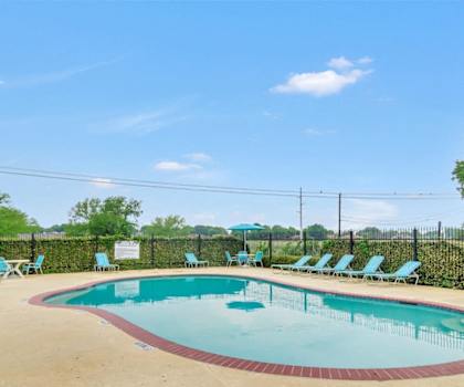 A pool surrounded by chairs and a fence.