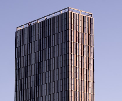 A tall building with a glass facade stands against a clear sky.