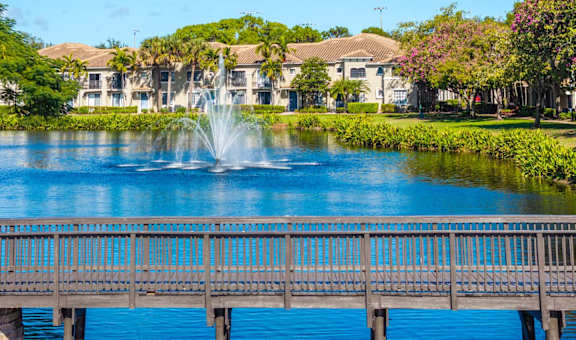 A bridge over a lake with a fountain in the middle of the lake.