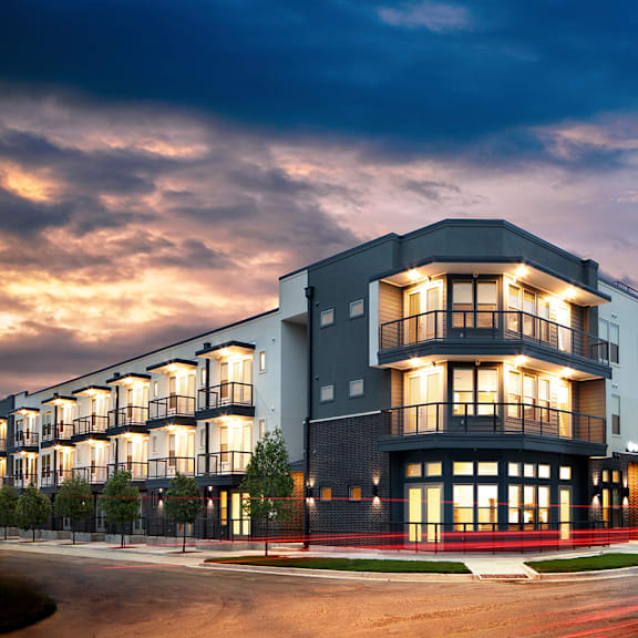 A modern apartment building with a curved facade and balconies is illuminated at dusk.