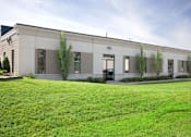 Thumbnail 1 of 5 - A building with a grey facade and greenery in front.