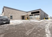 Thumbnail 1 of 5 - A building with a grey truck parked in front.