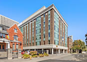 Thumbnail 1 of 4 - A modern glass building is situated in front of a red brick building.