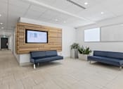 Thumbnail 4 of 4 - A modern waiting room with a TV on the wall and two blue sofas.