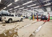 Thumbnail 4 of 5 - A white truck is parked in a garage with a car on a lift.