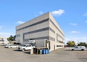 Thumbnail 10 of 13 - A large grey building with a parking lot in front.