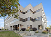 Thumbnail 1 of 13 - A modern building with a beige facade and large windows.