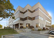 Thumbnail 8 of 13 - A modern building with a symmetrical design and a parking lot in front.