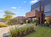 Thumbnail 5 of 6 - A modern building with a glass facade and a landscaped front yard.