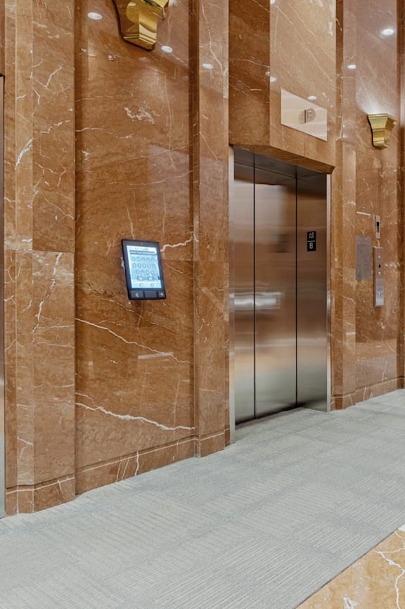 A long hallway with marble floors and walls, and a row of elevators on the left side.