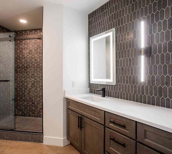 A bathroom with a brown tile shower and a white sink.