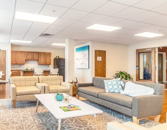 a community room with  a gray couch and white chairs and a kitchenette at Villas on the Strand apartments in Galveston, TX