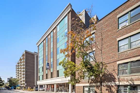A modern building with a glass facade is surrounded by trees with autumn leaves.