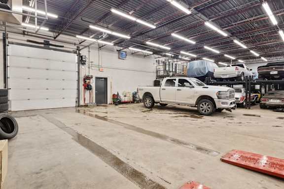 A white truck is parked in a garage with a red mat on the floor.