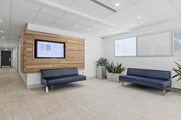 A modern waiting room with a TV on the wall and two blue sofas.