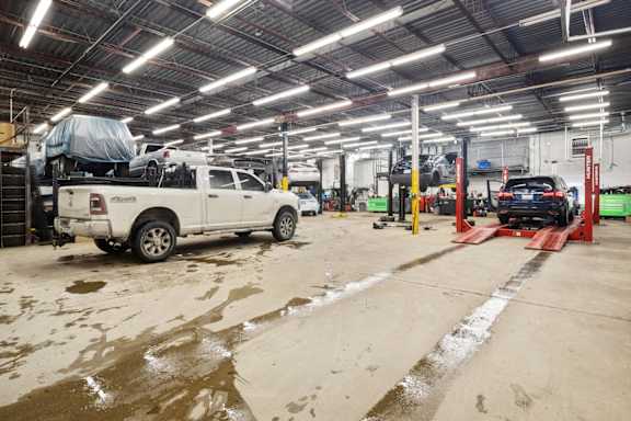 A white truck is parked in a garage with a car on a lift.