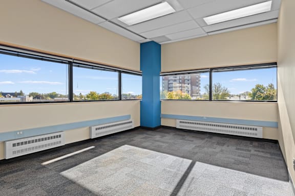 A room with a blue column in the middle and a large window with a view of the city.