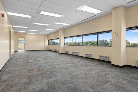A large, empty office space with carpeted floors and large windows.