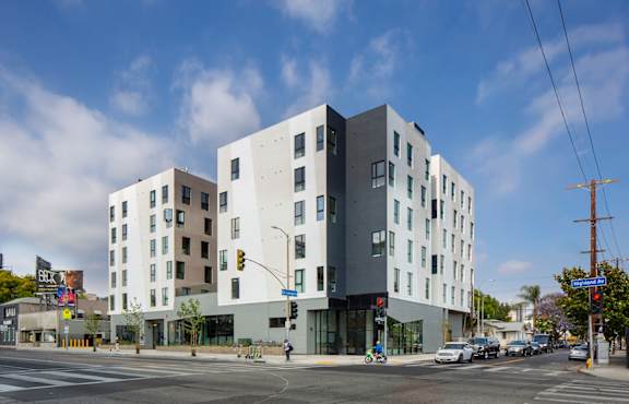 A modern building with a white and grey exterior is situated on a street corner with cars and traffic lights.