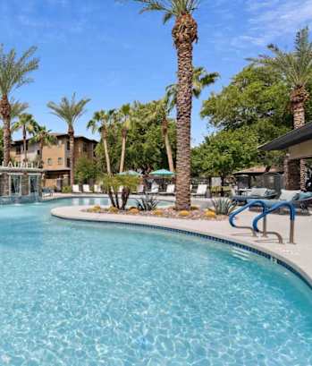 A large swimming pool surrounded by palm trees and lounge chairs. at The Laurel Apartments, Chandler