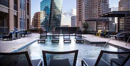 A pool with chairs around it in the foreground with buildings in the background. at Uptown by Onni Apartments, Apartments, Dallas, TX