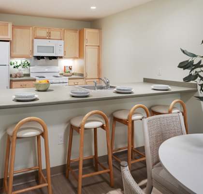 A kitchen with a white refrigerator, wooden cabinets, and a counter with bar stools.