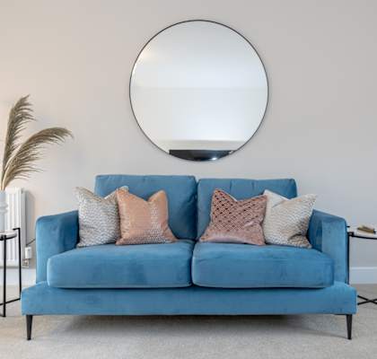 A blue couch with pillows and a round mirror above it.
