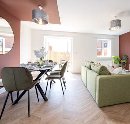 A modern living room with a green sofa and a dining table with chairs.