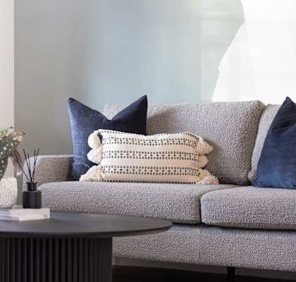 A grey couch with a white pillow and a plant on a table.