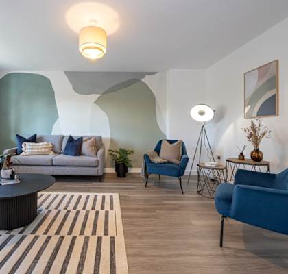 A living room with a grey couch, blue chairs, and a striped rug.