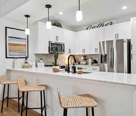 A kitchen with white cabinets and a white island with two barstools. at The Laurel Apartments, Chandler