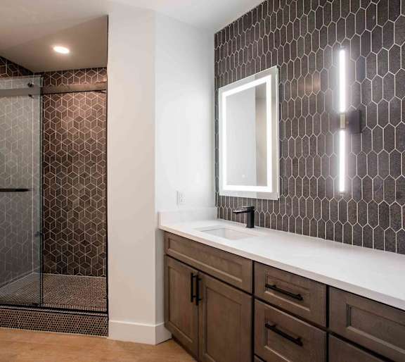 A bathroom with a brown tile shower and a white sink. at The Laurel Apartments, Chandler, AZ