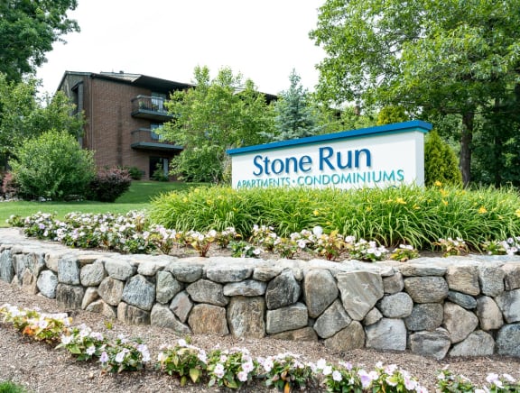 a stone wall with flowers and a sign that says stone run apartments condominiums