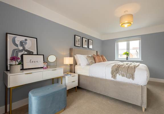 A bedroom with a bed, nightstand, and a desk with a lamp and a vase of flowers.