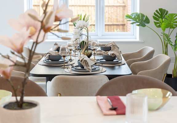 A dining table set with plates and glasses with a potted plant on the side.