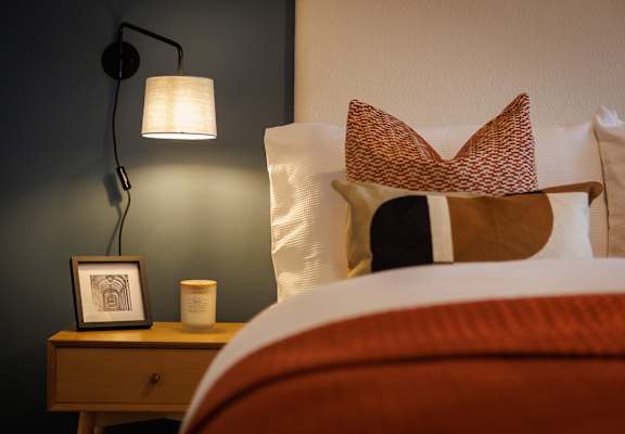 a bed with pillows and a lamp and a picture on a night stand