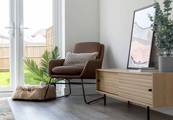 A brown chair with a pillow is in front of a mirror and a plant.